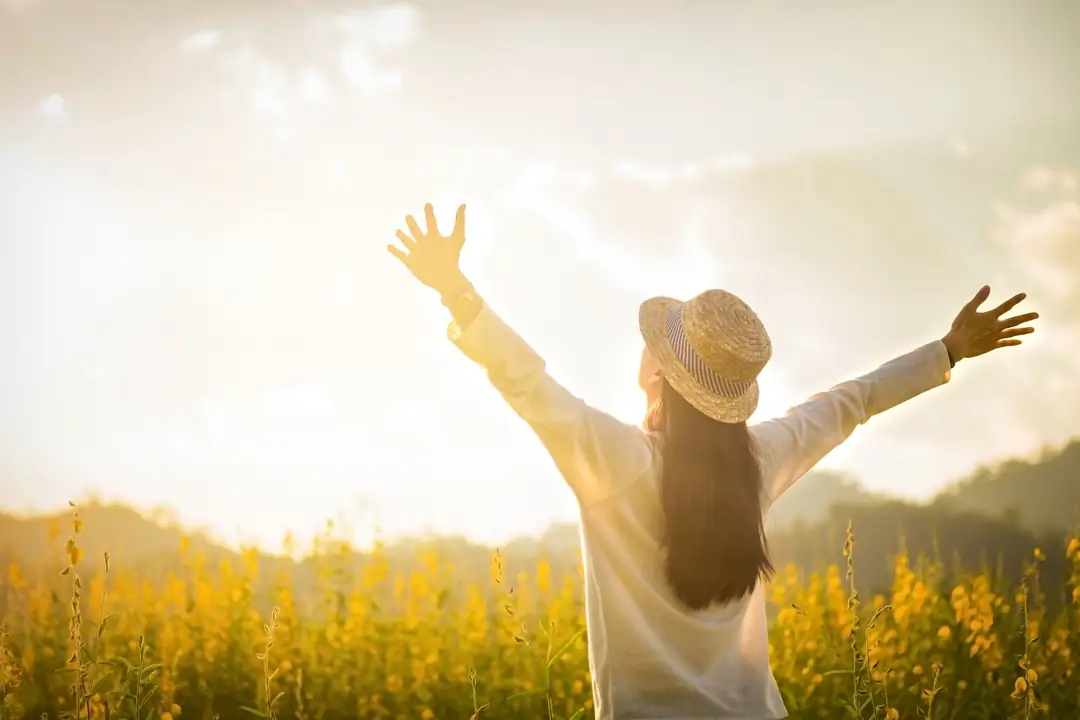 Woman in a sun hat raising her arms in a sunny field